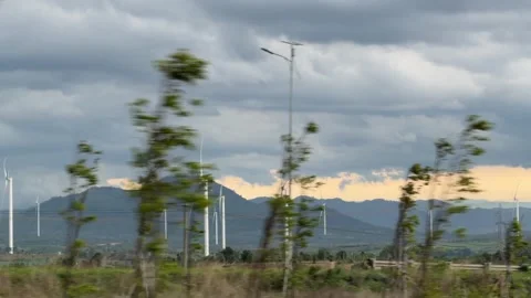 Wind turbines stand across an open field with a mountain range and cloudy sky vi 库存影片 339279911