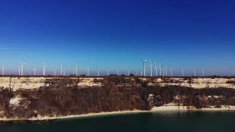 Wind turbines stand along the edge of a cliff near a calm body of water Stock-Footage 336542229