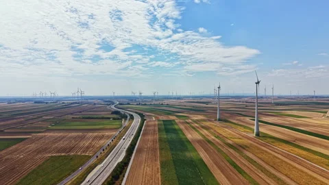 Wind turbines stand among fields in a rural area with a highway running through Stock Footage 342722839
