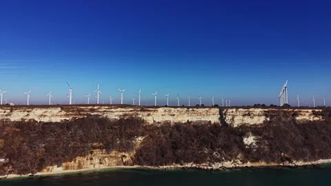 Wind turbines stand on the cliff edge near the coast at midday Vidéo 336542241