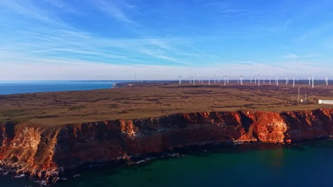 Wind turbines stand on cliffs beside the ocean under a blue sky during daylight Stock Footage 332021911