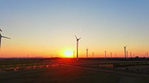 Wind turbines stand in a field during sunset with a bright sky and distant hills Stock Footage 344259054