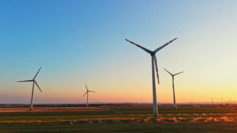 Wind turbines stand in a field during sunset with clear sky in the background Stock Footage 344260109