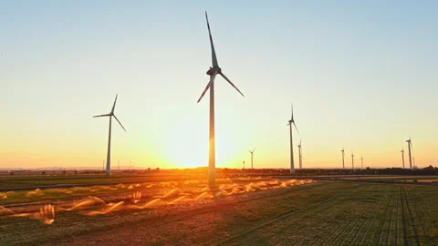 Wind turbines stand in a field during sunset with water sprinklers spraying in Stock Footage 344263798