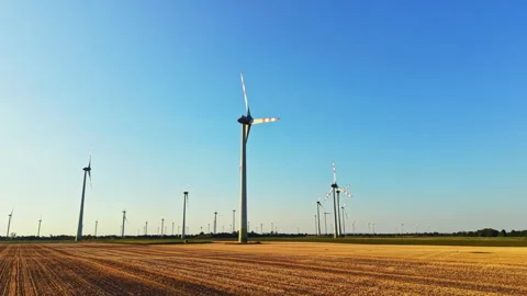 Wind turbines stand in a field under a clear sky during the day in an open area Stock Footage 344269356