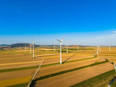 Wind turbines stand in fields with clear skies in a rural area during daytime Stock Photos