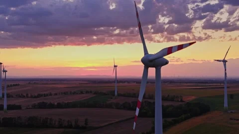 Wind turbines stand in fields during sunset with clouds in the sky Stock Footage 343123191