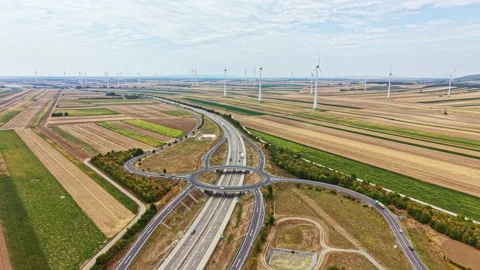 Wind turbines stand in fields near a roundabout highway in a rural area during a Stock Footage 342785032
