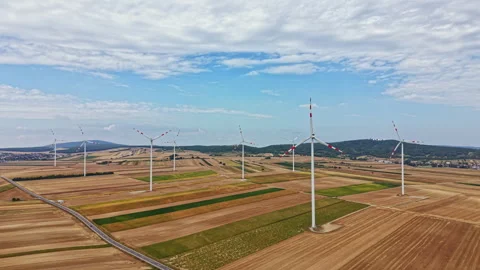 Wind turbines stand in fields under a blue sky with clouds in an open area Stock Footage 342731031