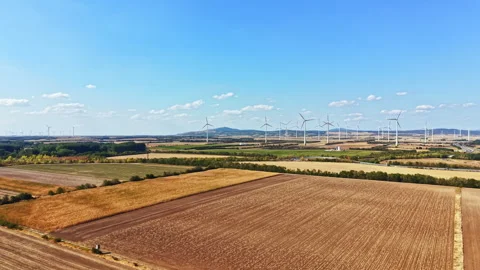 Wind turbines stand in fields under a blue sky during the day, creating energy Stock Footage 342733190