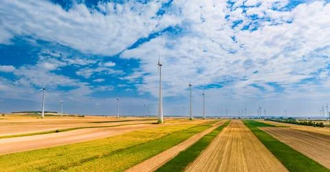 Wind turbines stand in fields under a blue sky with scattered clouds. Wind .. Stock Photos