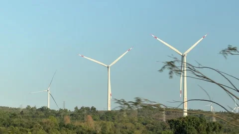 Wind turbines stand on a hill recorded from a moving vehicle while passing Stock Footage 335276643
