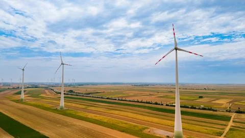 Wind turbines stand in open fields under a cloudy sky in rural area. Wind t.. Stock Photos