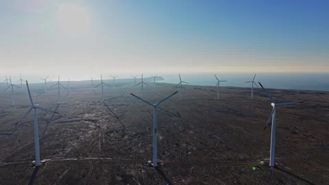 Wind turbines stand on open land near the coast on a sunny day Stock Footage 336541725