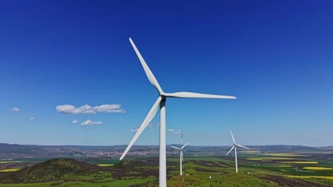 Wind turbines stand tall in a clear blue sky over green fields Stock Footage 338275258