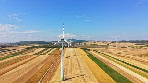 Wind turbines stand tall on fields under a blue sky with some clouds in a rural Stock Footage 342725560