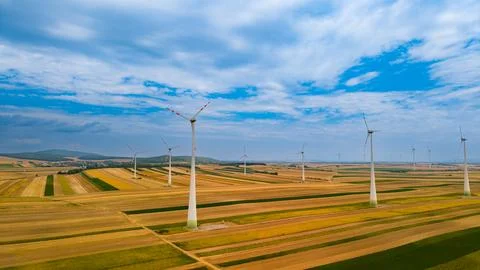 Wind turbines stand tall in fields under a blue sky. Wind turbines spin in .. Stock Photos
