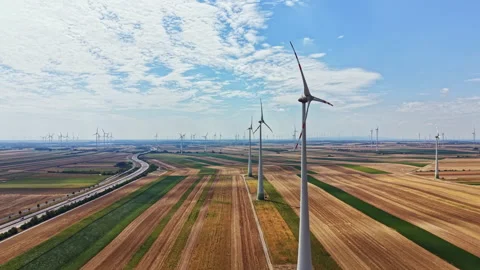 Wind turbines stand tall in a flat landscape with fields and a road below on a Stock Footage 342723174