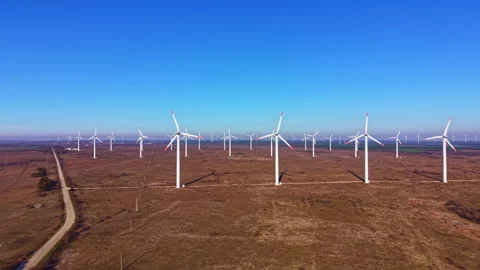 Wind turbines stand tall in an open field under a clear blue sky during daylight Stock Footage 336636942