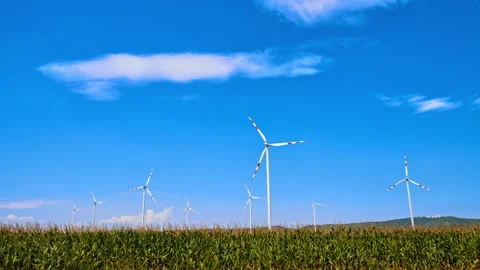 Wind turbines stand tall over a cornfield on a sunny day. Wind turbines spin 動画素材 342736434