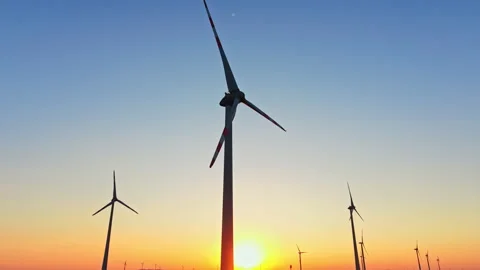 Wind turbines stand tall at sunset in a field, capturing renewable energy with Stock Footage 344259722