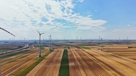 Wind turbines stand tall in a vast landscape under a clear sky with fields Stock Footage 342724060