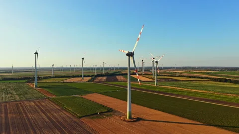 Wind turbines standing in a large field on a sunny day with clear skies as they Stock Footage 344268697