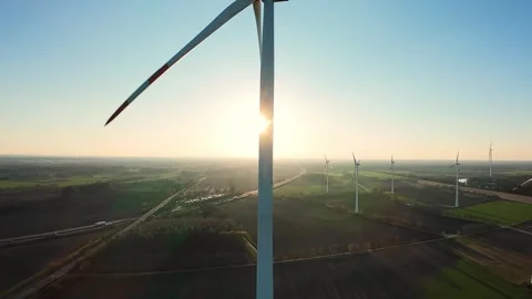 Wind turbines at sunset with sun flare behind rotating blade in a sustainable Stock Footage 325825428