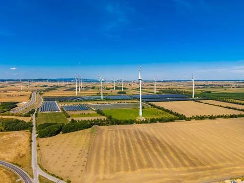 Wind turbines turn in the distance while solar panels reflect sunlight in a r Stock Photos