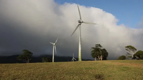 Wind turbines turning in the sunshine while a storm brews in the background Stock Footage 265918127