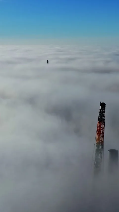 Wind turbines under construction emerging from a dense fog bank under a clear Stock Footage 339646683