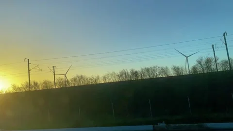 Wind turbines visible while driving on the road at sunset Vídeos de archivo 258278260
