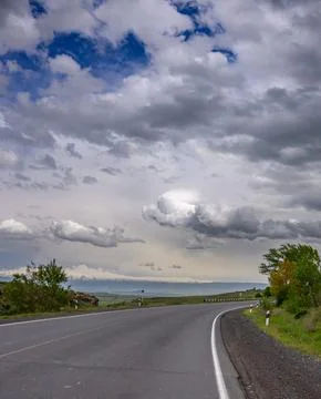 Winding asphalt road under dynamic sky with scattered clouds Stock Photos