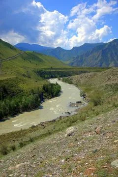 The winding bed of a turquoise river flows at the foot of high mountain range Stock Photos