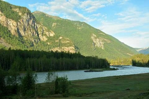 The winding bed of a wide river in the shadow of a mountain flows along mou.. Stock Photos