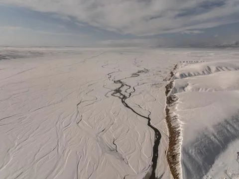 Winding dark river through vast snow-covered frozen plains Photos