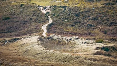 A winding dirt path through grassy hills on a sunny day Stock Photos