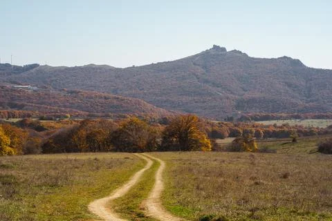 Winding dirt path through vibrant autumn landscape with distant mountains under Stock Photos