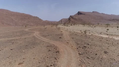 Winding Dirt Trail Through Rocky Desert Valley with Mountains Morocco Stock Footage 335033673