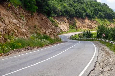 Winding mountain road bordered by lush greenery and exposed earth Stock Photos