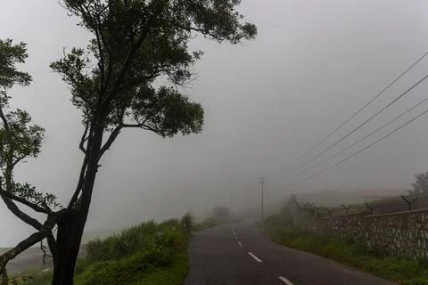 Winding mountain road bordered by a stone wall disappearing into thick fog Stock Photos