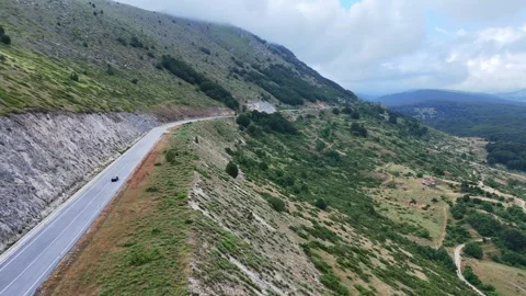 Winding Mountain Road Surrounded by Lush Greenery Under a Dramatic Cloudy Sky Video stock 281276662