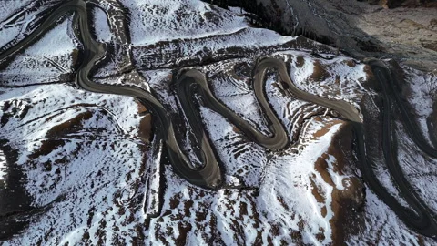 Winding mountain road switchbacks through snowy hills aerial view Stock Footage 324972522