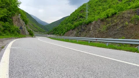 Winding mountain road through lush green valley under cloudy sky Stock Footage 310246122