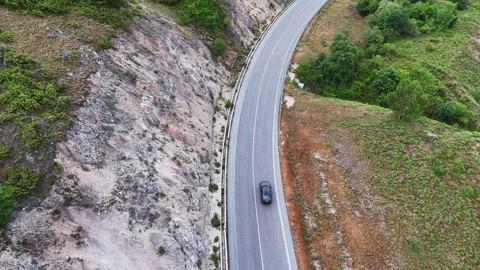 Winding Mountain Road Underneath Soft Clouds With a Car Navigating Around Green Stock Footage 281285873