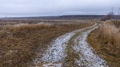 A winding path cuts through a serene winter landscape of snow and grass patch Stock Photos