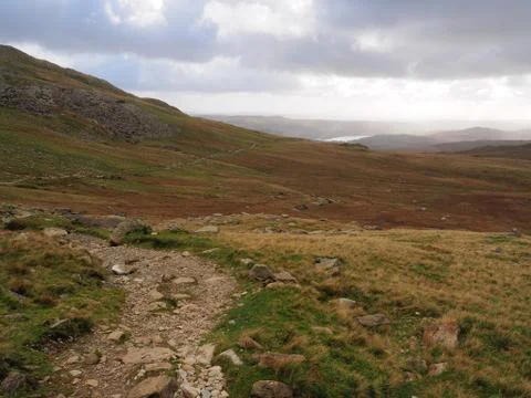 Winding path over mountains with Coniston Water in distance, Lake District Stock Photos