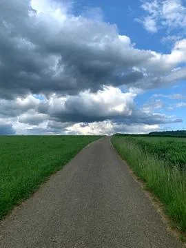 A winding pathway cuts through lush green fields under a dramatic sky fille.. Stock Photos