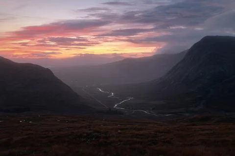 A winding river between mountain ranges illuminated by the rising sun Stock Photos