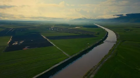 Winding river cuts through lush green fields 스톡 동영상 332440453